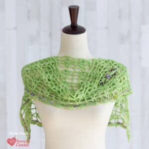 Springtime Violets Wraplet crochet pattern — spring green open lace shoulder wrap with multicolor speckled trim and purple gemstone brooch on dress form, American Crochet