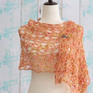 Amber Rose Wrap crochet pattern — open lace mesh wrap in warm peachy coral on dress form, American Crochet